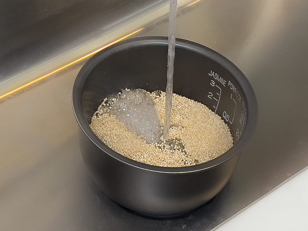 Adding water to a rice cooker pan with quinoa in it 