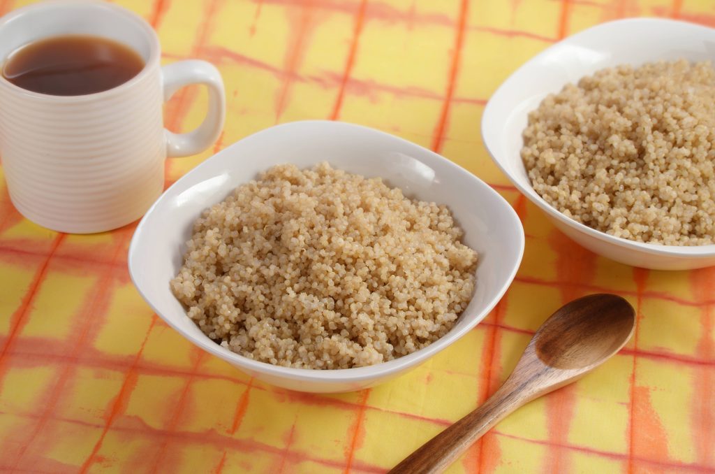 Cooked quinoa in a white bowl on the yellow and orange table cloth with hot tea on the side.