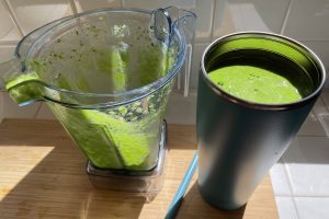 empty blender sitting next to cup full of green smoothie