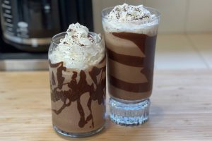 two coffee milkshakes in tall glasses on wooden surface