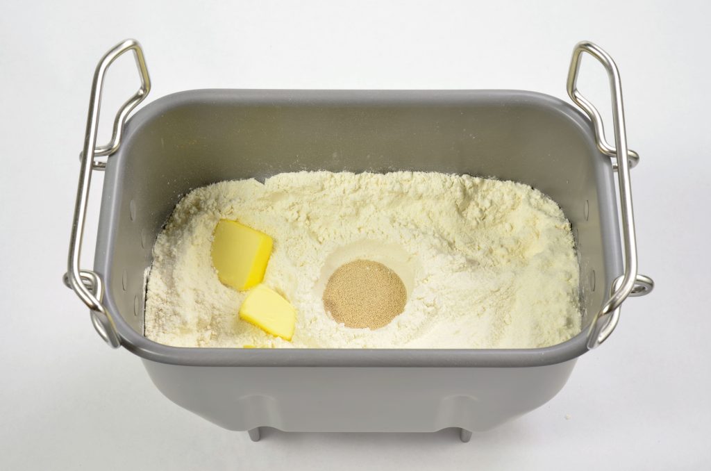 Bread ingredients in the breadmachine pan in a white background