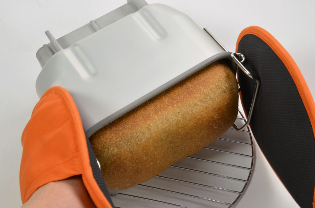 Holding pan with orange mittens to remove the baked bread from the pan