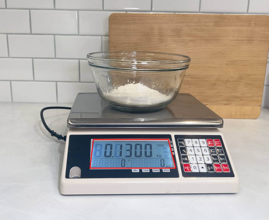 Flour in a glass bowl on a kitchen scale that reads 130 grams