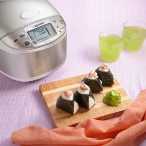 3 onigiri on a wood tray next to a rice cooker and 2 cold ice green tea