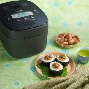 3 Mushroom miso onigiri on a wooden plate next to black rice cooker and hot green tea